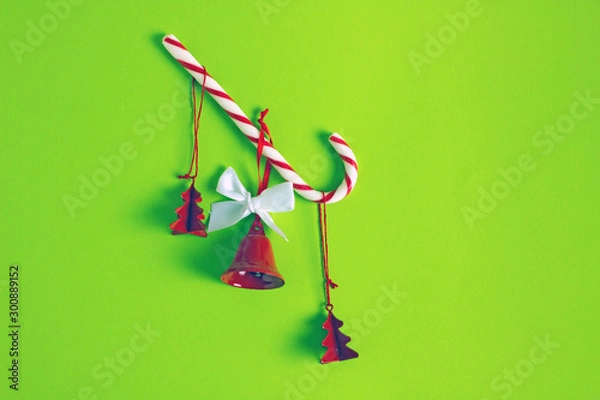Fototapeta Composition of  christmas minimalism on a green background. Red Christmas tree toys and bells and candy cane.