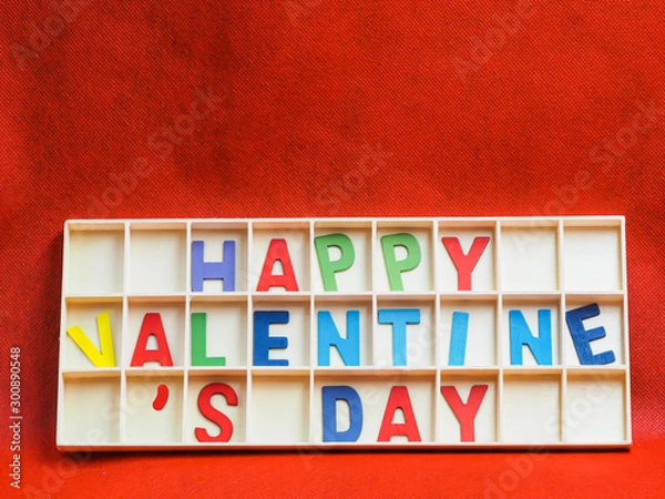 Fototapeta Multicolored wooden alphabets or letters of happy valentine 's day texts or words in wooden grids box on rough vivid or vibrant gradient red paper texture and background.