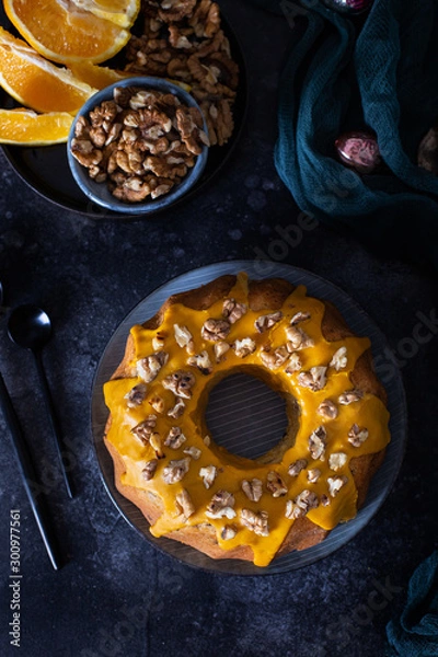 Fototapeta Bundt cake, orange cake with walnuts and yellow sugar icing with turmeric spice. Dark background. View from above