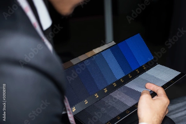 Fototapeta The dressmaker is choosing the fabric to cut the suit. Customers are choosing the color of the fabric in order to tailor the suit.