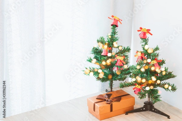Fototapeta Two small Christmas trees decorated with lights And the gift box on a wooden table that is placed in the corner of the room.