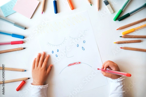 Fototapeta Child drawing sad face on the paper. Close up hands and picture.