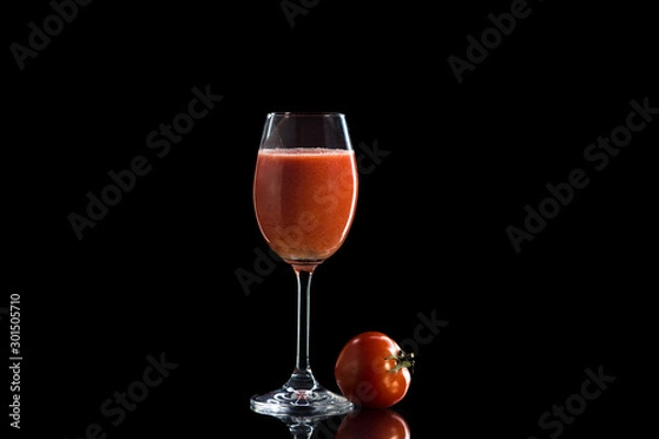 Fototapeta a glass of tomato juice stands on a reflective surface on a dark background and next to it lies a red round tomato.