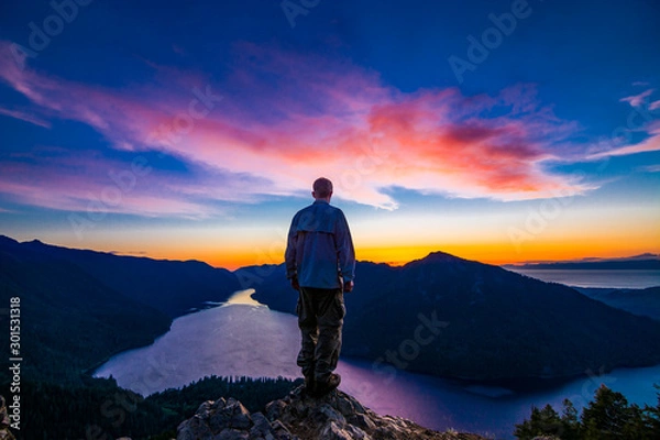 Fototapeta Adventurous man watching a sunset from a mountaintop.