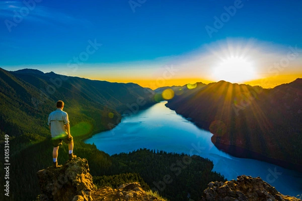 Fototapeta Adventurous man watching a sunset from a mountaintop.