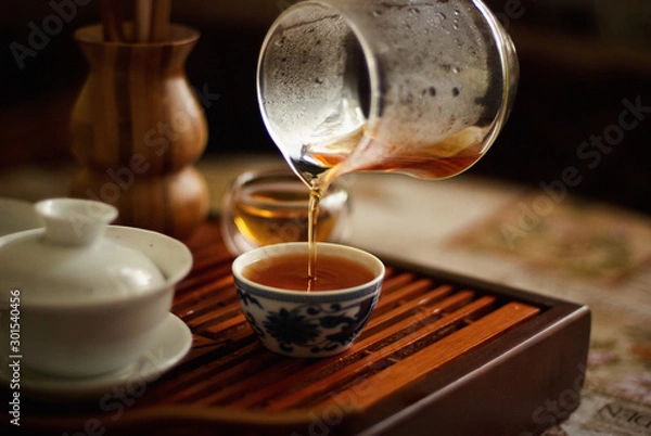 Fototapeta At a tea ceremony black tea is poured from a glass into a small Cup