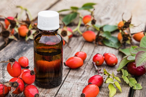 Obraz Bottle of rosehip seed essential oil and fresh red berries on a wooden table. Tincture or essential oil with rose hips.