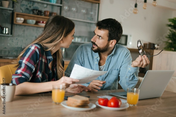 Fototapeta Young couple arguing while having problems with their home finances at dining table