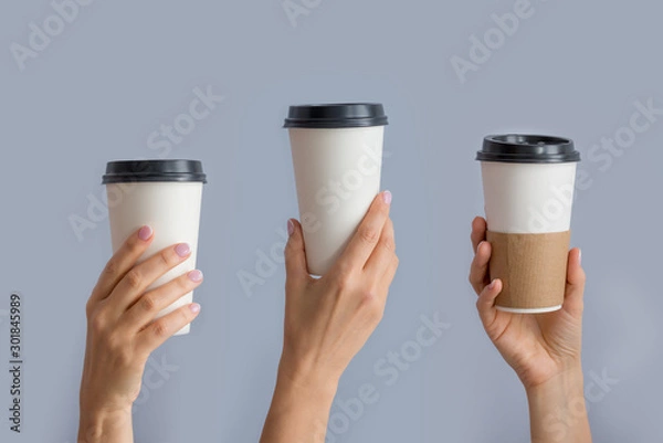 Fototapeta Mockup of several female hands holding up a Coffee paper cup isolated on grey background. Front view
