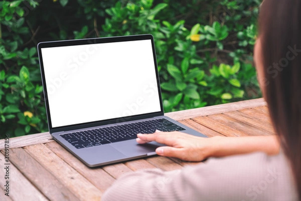 Fototapeta Mockup image of a woman using and touching on laptop touchpad with blank white desktop screen on wooden table