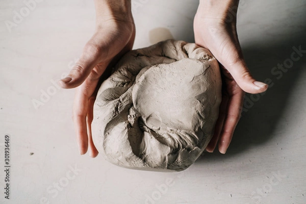 Fototapeta Female potter hands working with clay in workshop. White desk on background