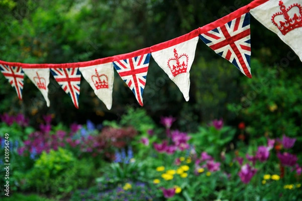 Fototapeta Banner of British Union Jack flag and royal crown celebratory bunting hanging in front of a flowery English summer garden background