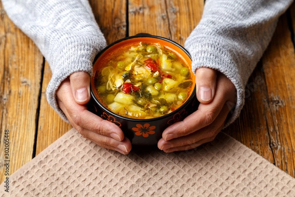 Obraz Female hands hold a plate with vegetable soup with chicken. Plate with soup and croutons on a wooden background. Healthy eating concept.
