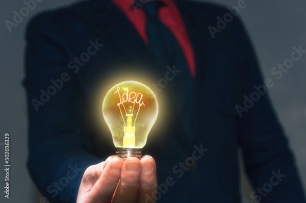 Fototapeta The businessman holds a lamp with a new idea in front of yourself. Concept of a new idea, new discovery.