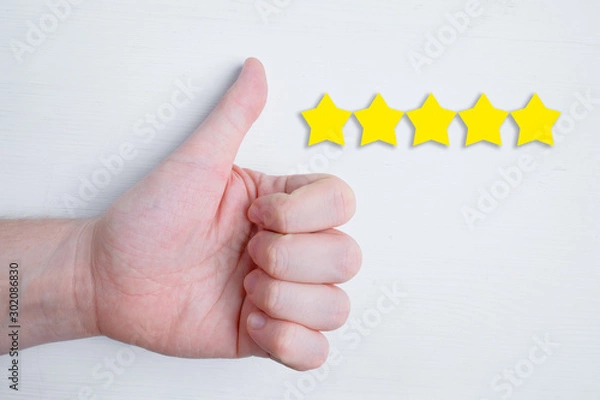 Fototapeta A man puts a like with a hand with a nearby five-star abstract rating on a white background. Best score. Flat lay.