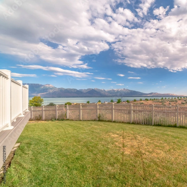 Fototapeta Square Bakyard with white wooden fence overlooking a scenic view of lake and mountain