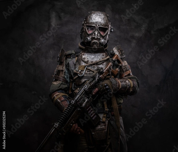 Fototapeta Concept of post - apocalypse futuristic warrior with weapon in hands at dark photo studio.
