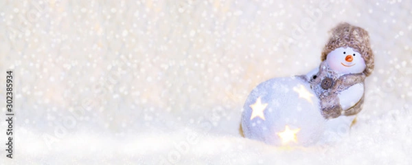 Obraz Picture for web banner. Toy snowman in a knitted hat, with a luminous ball close up on a white background. New Year and Christmas background for greetings, banner, postcard, advertisement, Copy space,
