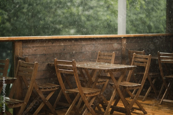 Fototapeta  it rains heavily in a cafe, there are no people on the terrace of wood, on which stands a wooden table, wooden chair, on a dark wooden floor