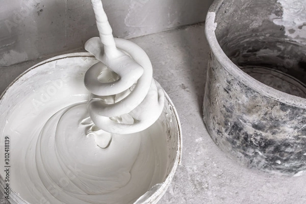 Fototapeta Plastic bucket with fresh putty, spiral whisk for electric building mixer soiled with putty and empty dirty bucket on raw concrete floor. Facing work and construction concept. Close-up