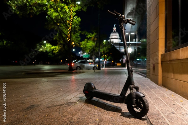 Fototapeta Modern Electric Scooter Parked in a Downtown Urban Setting at Night