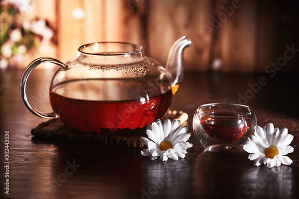 Obraz Glass teapot with tea on a dark background with flowers