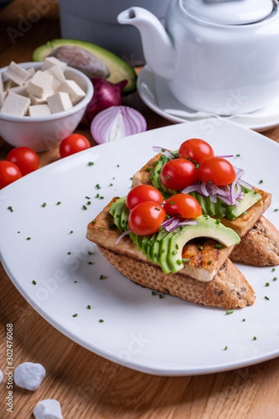 Obraz Vegan sandwich with grilled tofu, avocado, cherry tomato, vegetables and scrambled tofu. Chef cooking. Vegan open sandwiche. Healthy food concept.