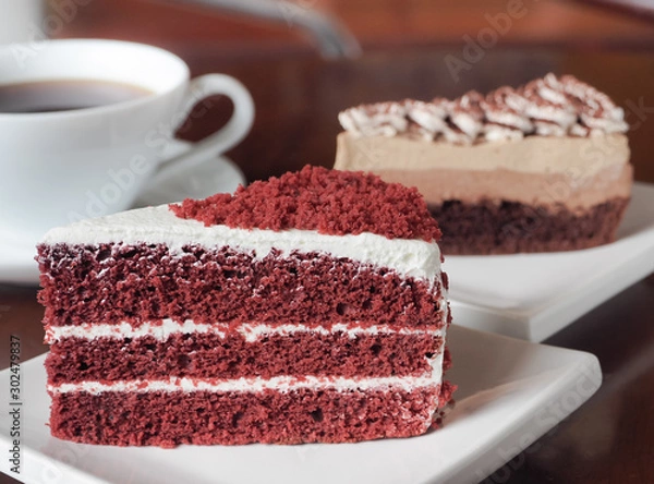 Obraz Slice of red velvet cake on a white plate. Close up of red velvet chocolate cake and tiramisu coffee cake with a cup of hot coffee on table.