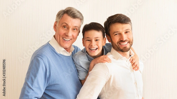 Fototapeta Smiling Boy, Father And Grandfather Hugging Standing Against White Background