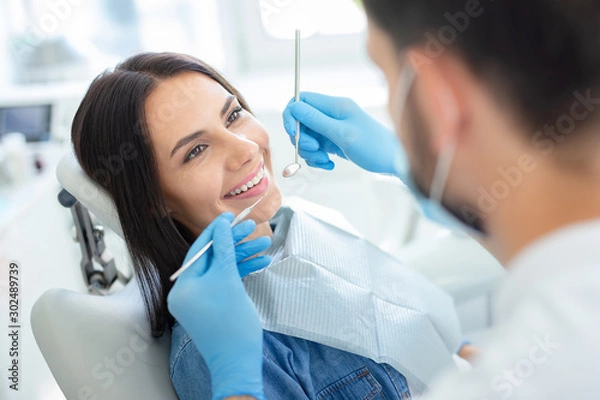 Fototapeta smiling happy client in dental chair with doctor looking her with instruments
