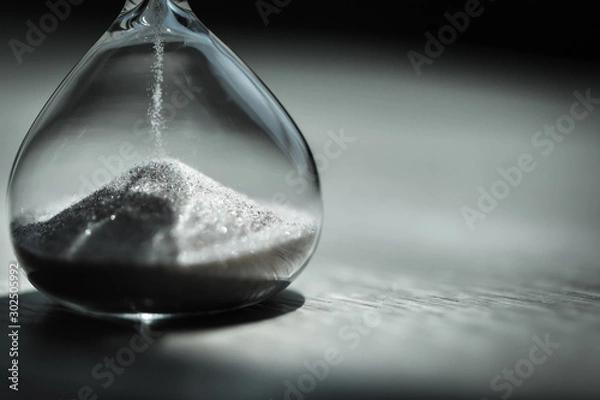 Fototapeta Sand running through the bulbs of an hourglass measuring the passing time in a countdown to a deadline, on a bright background with copy space.