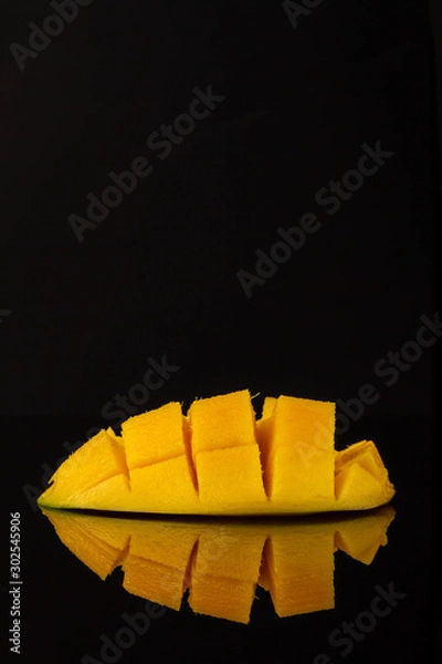 Fototapeta Ripe yellow mango slice on a mirror black table. Mango with reflection.