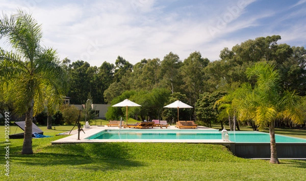 Obraz Beautiful view of a swimming pool in a sunny day. Gardens of a typical countryside lodging (estancia), perfect for a romantic getaway next to the city. Colon, Entre Rios, Argentina