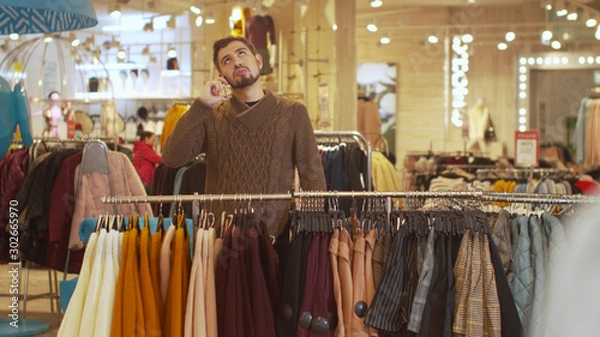 Obraz Young guy discusses clothes on the phone in a store