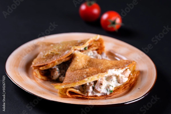 Obraz Delicious crepes pancake with champignon cream, chicken, mushrooms fresh green herbs and white cheese on plate, black background. Top view homemade breakfast. Russian national food.