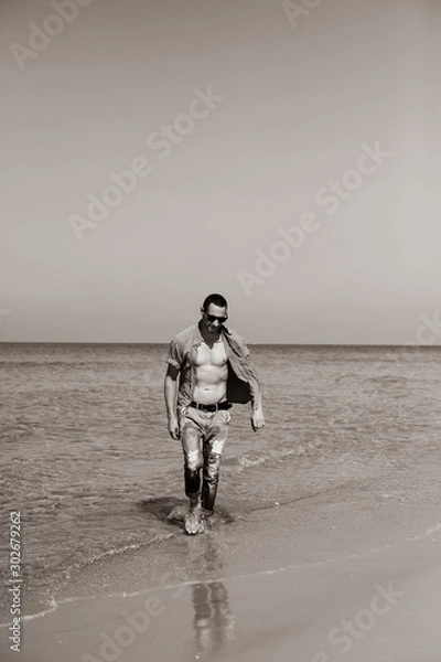 Obraz young muscular man resting and posing on the beach. A young man walks by the sea