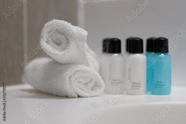 Fototapeta Mini bottles with cosmetic products and towels on table, space for text. Hotel amenities