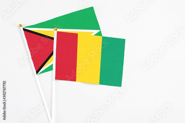 Fototapeta Guinea and Guyana stick flags on white background. High quality fabric, miniature national flag. Peaceful global concept.White floor for copy space.