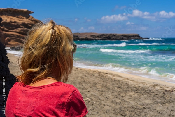 Obraz A woman with blond hair sits on the beach and has the view of the sea