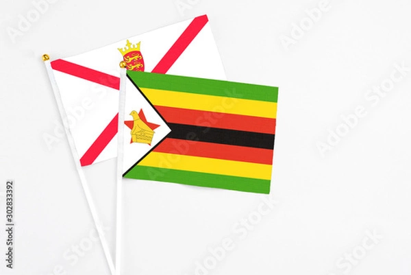 Fototapeta Zimbabwe and Jersey stick flags on white background. High quality fabric, miniature national flag. Peaceful global concept.White floor for copy space.
