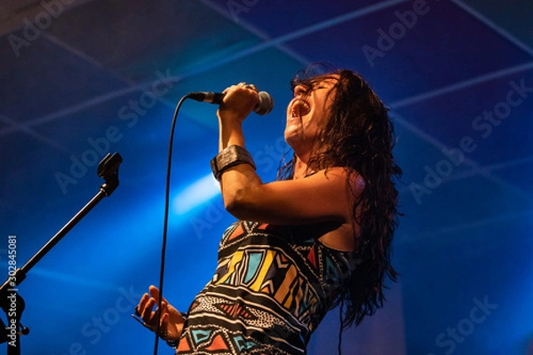Fototapeta A female musician is viewed from a low angle as she sings, with open mouth in microphone during a performance on stage