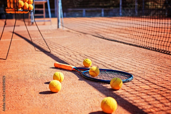 Fototapeta Tennis racket and balls laying on the ground in the shadow of the net