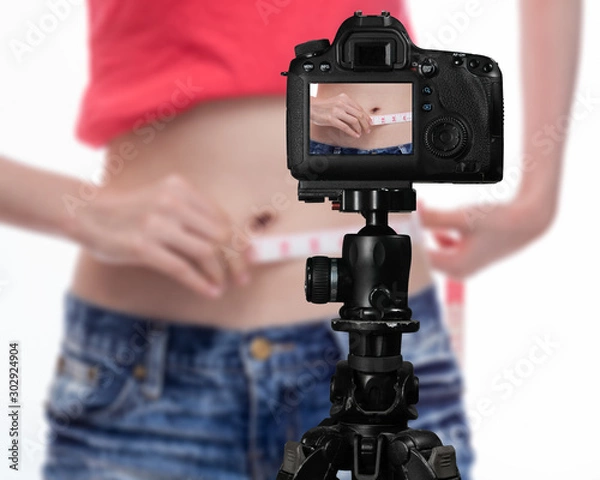 Obraz Asian vlogger measuring waist behind camera, social media concept