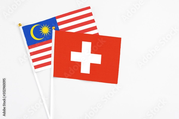 Fototapeta Switzerland and Malaysia stick flags on white background. High quality fabric, miniature national flag. Peaceful global concept.White floor for copy space.