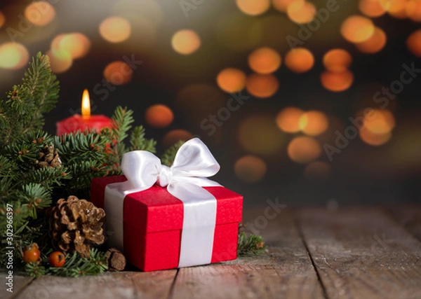 Fototapeta Gift box and fir branches with candles on wooden table. Background bokeh yellow lights