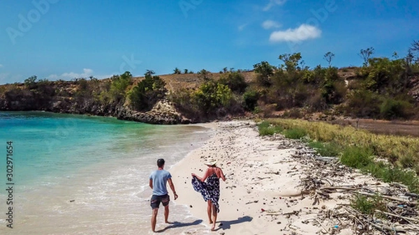 Fototapeta A couple walking on the Pink Beach in Lombok, holding hands. This place is a hidden gem, not spoiled by tourists. Solitude and calm feelings, waves gently spreading on the beach.