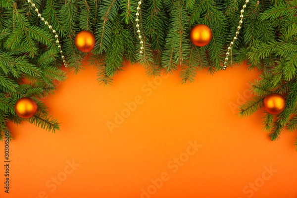 Fototapeta Orange christmas card with free space. branches of spruce with balls on an orange background