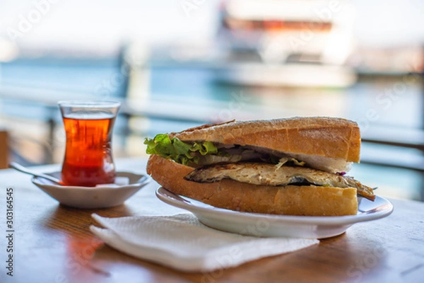 Obraz Istanbul fish sandwich. Burger with fried fish. Turkish tea with Balik Ekmek. Blurred background with sea view