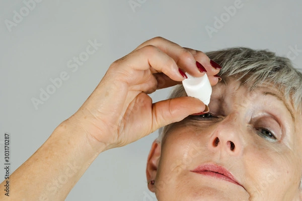 Obraz older woman looking up applying eye drops on White background