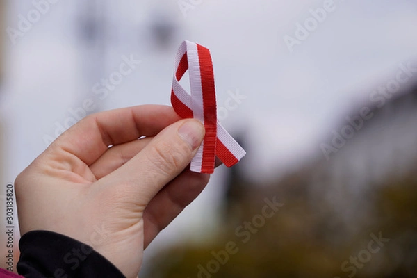 Fototapeta hand with red and white ribbon on background. Flag background national holiday country november celebration.1 of May, November 11, flag or independence or labor day. Government holiday in poland.